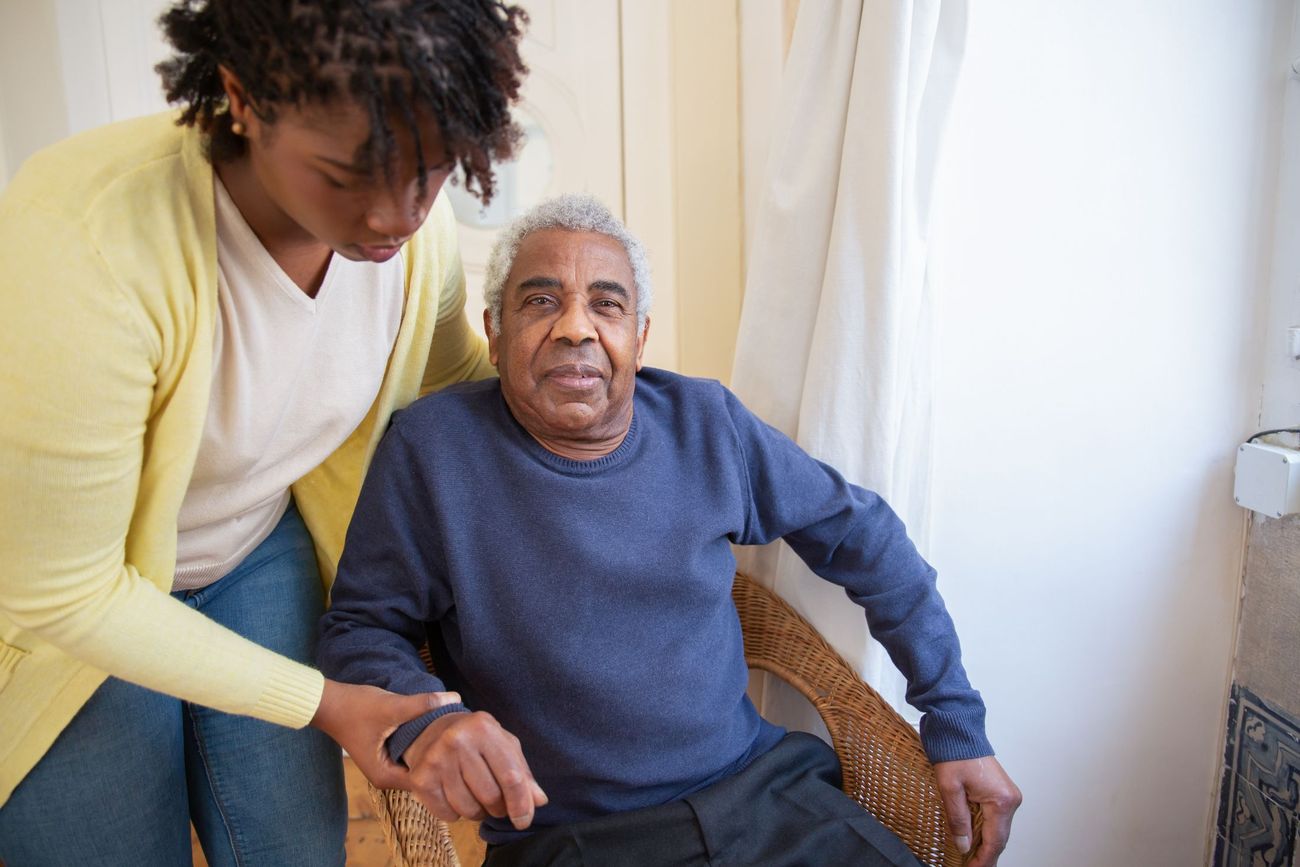 A support worker helping an older man rise from his armchair