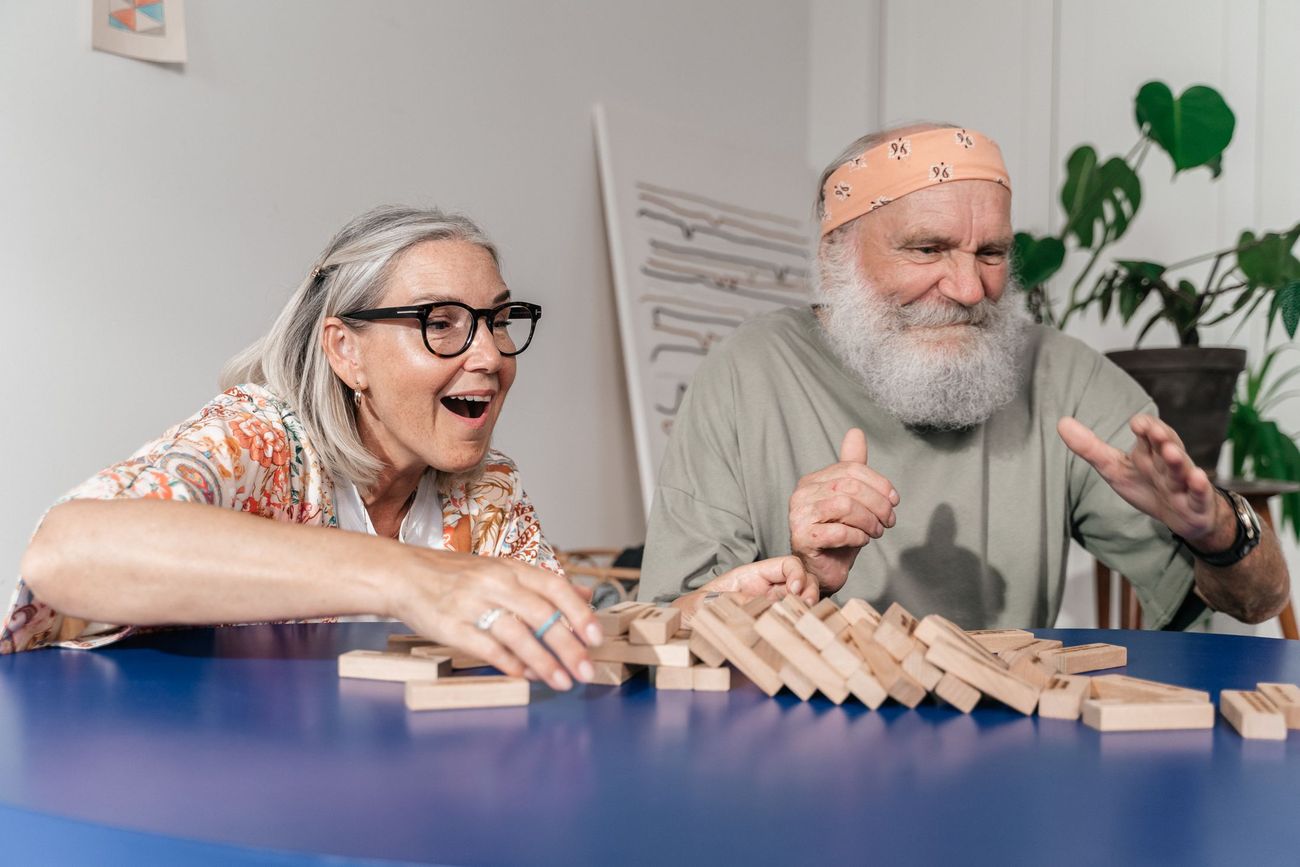 An older couple laughing together over a game at the kitchen table